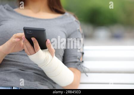 Nahaufnahme einer Genesungsfrau mit Bandarm am Telefon, die auf einer Bank im Park sitzt Stockfoto