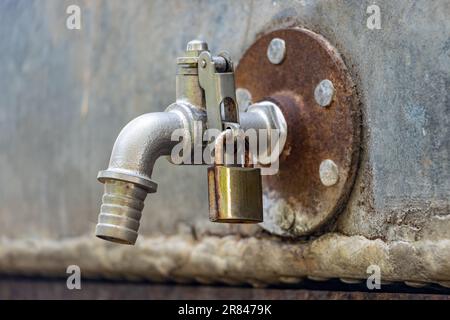 Ein Wasserhahn an der Zisterne, verschlossen mit einem Vorhängeschloss, Nahaufnahme Stockfoto