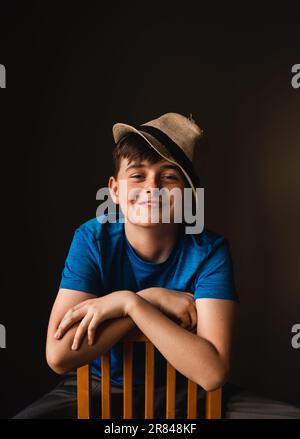 Porträt eines glücklichen Jungen mit Fedora-Hut, der rückwärts auf dem Stuhl sitzt. Stockfoto