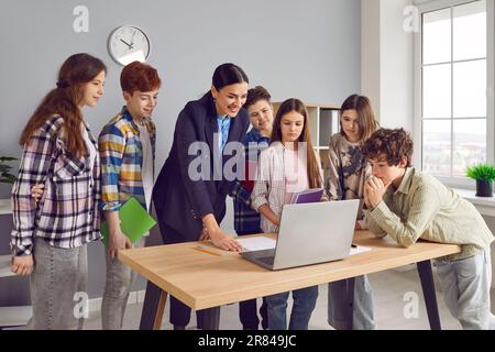 Gruppe von Klassenkameraden, die im Klassenzimmer neben ihrem Lehrer stehen und auf den Bildschirm des Laptops schauen. Stockfoto