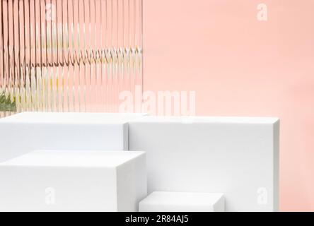 Weißer Blockfuß mit pfirsichfarbenem Hintergrund mit modernem Transparentstreifen-Glas und Blume mit Sonnenlicht Stockfoto