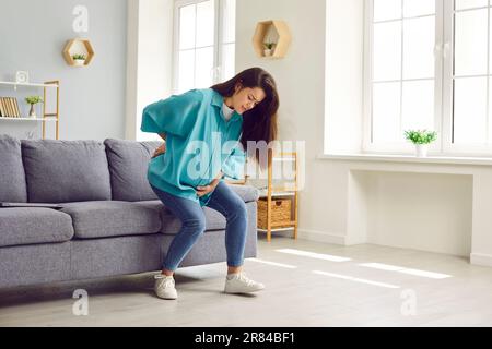 Schwangere junge Frau, die zu Hause Rückenschmerzen hat oder eine Geburt hat. Stockfoto