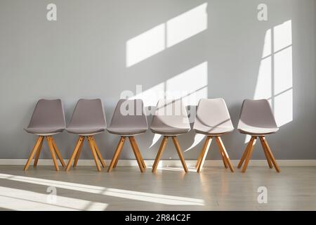 Sechs graue Stühle stehen in einer Reihe an der Wand in einer leeren Bürolobby oder einem Wartezimmer Stockfoto
