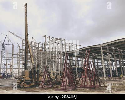 Bau eines Neukomplexes im Werk. Metallkonstruktionen für den Fundamentbau. Gelber Kran transportiert schweres Material durch die A Stockfoto