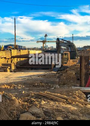 Portalkran, um eine U-Bahn im Stadtzentrum zu errichten. Der Kran gräbt Erde, Sand und Steine, um eine Bahnlinie unterirdisch zu bauen. Gelber heller Kran auf einem B Stockfoto