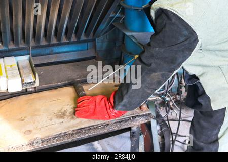 Ein männlicher Arbeiter, ein Schweißer in beruflicher Arbeitskleidung, arbeitet auf einem Schweißtisch für die Reparatur und Herstellung von Teilen und Ersatzteilen. Stockfoto