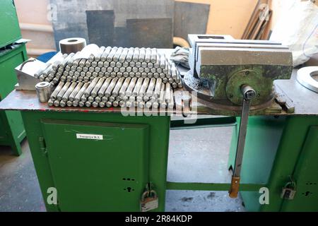 Viele glänzende Metallbolzen mit Schnitzereien, Muttern, Eisenringen, Dichtungen, Metallwerkzeugen und Industriegriffen auf dem grünen Robotertisch in der Fabrik, in der Werkstatt. Stockfoto