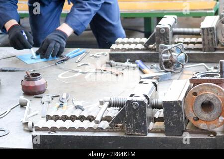 Der Arbeiter arbeitet auf einem Tisch mit einem Metallwerkzeug in der Fabrik. Konzeptindustrie, Arbeit in der Fabrik, Messen der Größe, Ausrüstung, INSPE Stockfoto