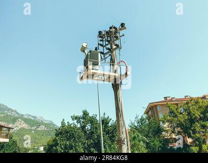 Stab mit Stromleitung. Elektrische Spulen auf schwarzen Kabeln, Kühlelemente. Säulen vor dem Hintergrund eines Berges in einem heißen, tropischen Land. Stockfoto