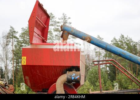 Das Korn aus dem Rohr fällt in eine große, rote Sägemaschine, einen Mähdrescher mit großen Rädern zum Pflügen des Bodens, eine Maschine zum Aussäen von Getreide, leistungsstark Stockfoto