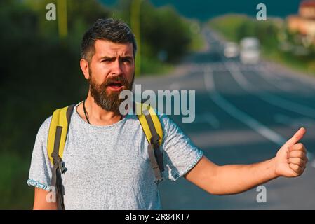 Auto-Stopp-Fahrt. Abenteuer- und Tourismuskonzept. Mann in legerer Kleidung winkt mit dem Auto und fährt am Straßenrand mit dem Anhalter. Reisen mit Autostop, mit Sommerausflug Stockfoto