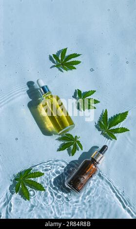 CBD-Ölflaschen, blauer Wasserhintergrund mit Tropfen, Wellen und Blättern aus Hanf, Marihuana Stockfoto