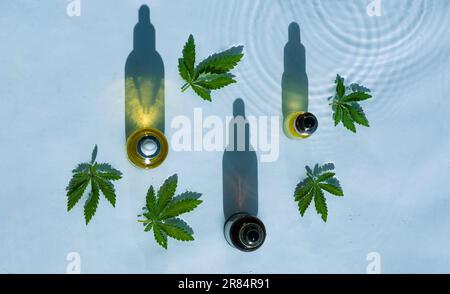 CBD-Ölflaschen, blauer Wasserhintergrund mit Tropfen, Wellen und Blättern aus Hanf, Marihuana Stockfoto