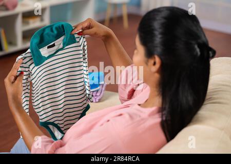 Schulteraufnahme einer glücklichen indischen schwangeren Frau, die zu Hause ein Baby fühlt, indem sie ein Kleid auf den Bauch legt - Konzept von Elternschaft, pränataler Verbindung und Stockfoto