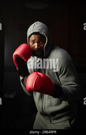 Ein junger afroamerikanischer Mann in roten Boxhandschuhen, der sich im Fitnessstudio vor der Kamera einen Boxsack ansieht und trainiert Stockfoto