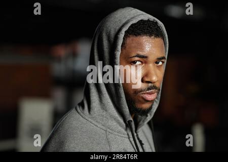 Junger ernsthafter afroamerikanischer Sportler oder Fitnesstrainer in grauem Hoodie, der im Fitnessstudio oder Sportverein in die Kamera schaut Stockfoto