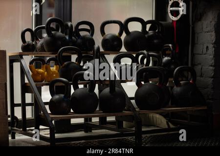 Großes Display mit schweren Kugelhanteln in Schwarz und Gelb auf Regalen in der Ecke des modernen Sportclubs oder Fitnessstudios Stockfoto