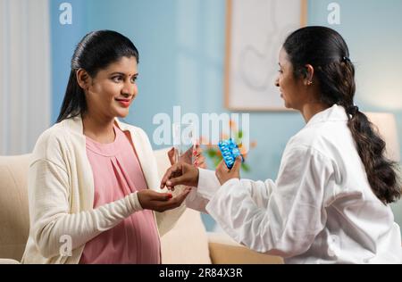 Schulterfoto der indischen Krankenschwester, die zu Hause eine schwangere Frau mit Pillen oder Medikamenten versorgt - Konzept der häuslichen Gesundheitsfürsorge, Krankenpflegeunterstützung und Mutterschaft Stockfoto