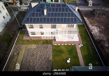 Draufsicht über das Haus mit Photovoltaik-Solarpaneelen auf dem Dach, umgeben von Hof-, Straßen- und Wohngebäuden. Haus mit Solarmodulen zur Stromerzeugung durch Photovoltaik. Stockfoto