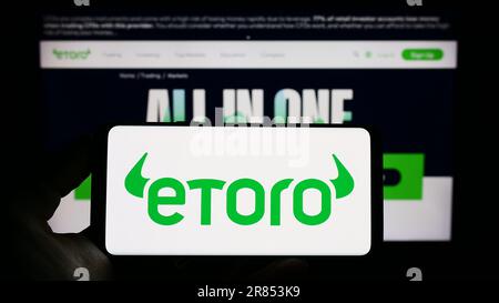 Person, die ein Mobiltelefon mit dem Logo des israelischen Social Trading Company eToro auf dem Bildschirm vor der Unternehmenswebseite hält. Konzentrieren Sie sich auf das Display des Telefons. Stockfoto