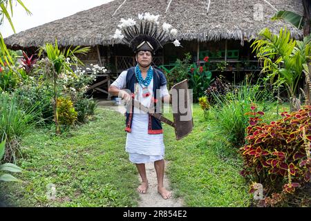 Ein Mann vom Adi-Minyong-Stamm aus dem Nordosten Indiens, gekleidet in traditioneller Kleidung, steht vor einem traditionellen Haus, Assam, Indien Stockfoto