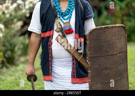 Ein Mann aus dem Stamm der Adi aus dem Nordosten Indiens, gekleidet in traditioneller Kleidung, mit einem speziellen Hut mit Federn, Dolch und einem Schild, Assam Stockfoto