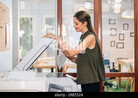 Vertrauensvolle Sekretärin, die mit modernen Druckern arbeitet und im Unternehmen arbeitet Stockfoto