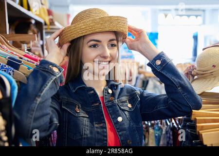 Junge Frau, Die Gebrauchte Nachhaltige Kleidung Aus Dem Second Hand Charity Shop Kauft, Versucht Auf Hut Stockfoto