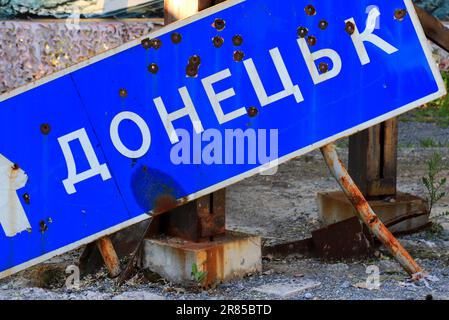 Russischer Krieg gegen die Ukraine, ukrainischer Krieg. Straßenschild mit Inschrift in Ukrainisch - Donezk, durchstochen von Kugeln und zerbrochen, Zerstörung in der Ukraine Stockfoto