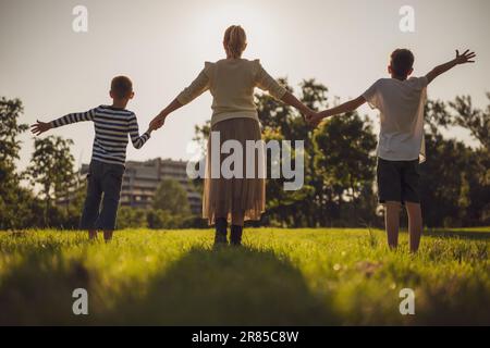 Glückliche Mutter spielt mit ihren Söhnen im Park. Sie halten Händchen und genießen den Sonnenuntergang. Stockfoto
