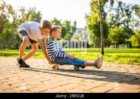 Zwei Jungs haben Spaß beim Skateboard im Park. Verspielte Kinder im Park, glückliche Kindheit. Stockfoto