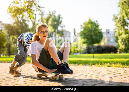 Zwei Jungs haben Spaß beim Skateboard im Park. Verspielte Kinder im Park, glückliche Kindheit. Stockfoto