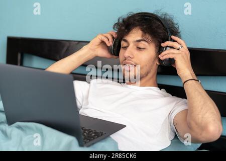 Ein junger arabischer Mann, der ein Notebook mit Kopfhörern benutzt und sich zu Hause im Bett einen Film ansieht. Werbung im Internet und Freiberufler im Bildungsbereich Stockfoto