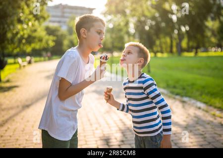 Zwei Brüder essen im Sommer Eis im Park. Sie amüsieren sich und verspotten sich. Stockfoto
