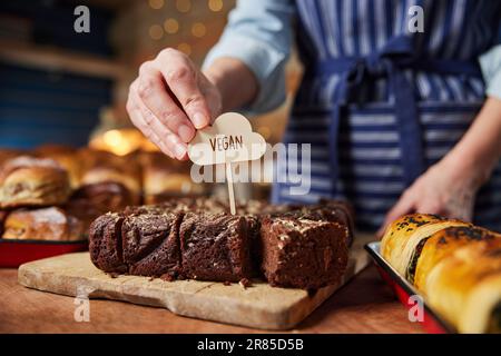 Verkaufsassistent In Der Bäckerei: Veganes Etikett In Frisch Gebackene Schokoladen-Brownies Geben Stockfoto