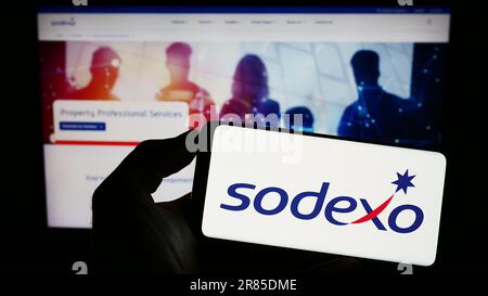 Person, die ein Mobiltelefon mit dem Logo des französischen Facility-Management-Unternehmens Sodexo S.A. auf dem Bildschirm vor der Webseite hält. Konzentrieren Sie sich auf das Display des Telefons. Stockfoto