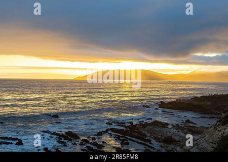 Sonnenuntergang am Pismo Beach in Kalifornien. Sonnenuntergang über den Bergen in der Nähe des Meeres. Dramatischer Sonnenuntergang über den Bergen und dem Meer. Sonnenstrahlen, die durch die Wolken filtern. Stockfoto