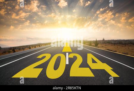 Das Wort 2024, das auf dem Highway geschrieben wurde. Ziel 2024 wird durch Pfeil auf einer leeren Asphaltstraße angezeigt. Wir kommen ins neue Jahr Stockfoto