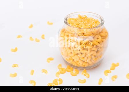 Ungekochte Chifferi Rigati Pasta in Glasglas auf weißem Hintergrund. Fett und ungesunde Lebensmittel. Verstreute Klassische Trockene Makkaroni. Italienische Kultur und Küche. Rohe Pasta Stockfoto