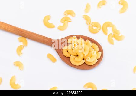 Ungekochte Chifferi Rigati Pasta in Holzlöffel auf weißem Hintergrund. Fett und ungesunde Lebensmittel. Verstreute Klassische Trockene Makkaroni. Italienische Kultur und Küche. Rohe Pasta Stockfoto