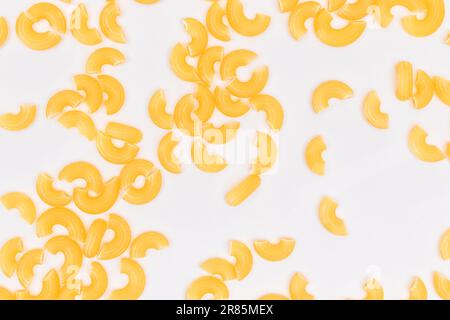 Verstreute ungekochte Chifferi Rigati Pasta auf weißem Hintergrund. Fett und ungesunde Lebensmittel. Klassische Trockene Makkaroni-Textur. Italienische Kultur und Küche. Rohe Pasta Stockfoto