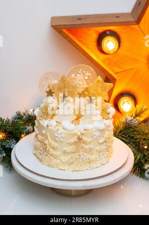 Festlicher goldener und weißer weihnachtskuchen mit cremigen weihnachtsbäumen, Lollipops, süßen Schneeflocken, Schokoladendekor, Glitzer und Streuseln Stockfoto