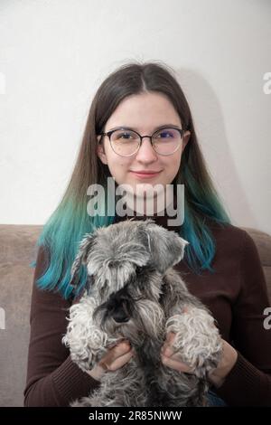 Porträt eines Teenagers mit langen braunen Haaren, Brille und einem grauen Schnauzer-Miniaturhund in der Hand. Ich kümmere mich um Haustiere. Haustiere Stockfoto