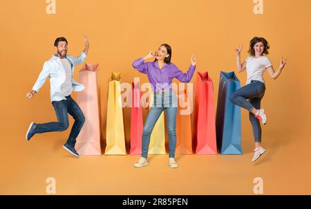 Emotionale, multiethnische junge Männer und Frauen durch riesige Einkaufstüten Stockfoto