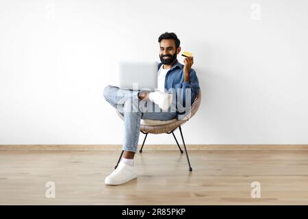 Arabic Guy Macht Einkaufen Mit Laptop Und Kreditkarte Drinnen Stockfoto