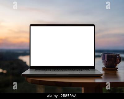 Laptop leerer Bildschirm auf Holztisch mit erstaunlichem Sonnenuntergangshimmel über Fluss Mockup. Clipping Path Gerät Bildschirm. Vorderansicht des Laptops aus silbernem Aluminium in der Nähe von Panoramafenstern mit Blick auf die Natur im Sommer Stockfoto
