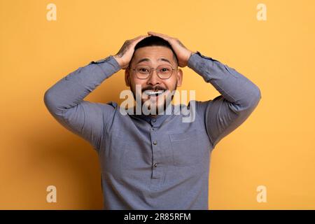 Porträt Eines Überraschten Aisan-Mannes, Der Den Kopf Berührt Und Den Mund Aufmacht Stockfoto