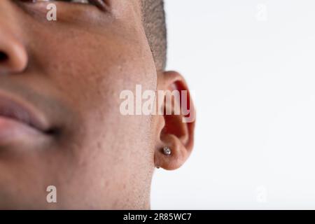 Scharfes Detail eines Ohrrings auf dem Ohr eines jungen schwarzen Mannes. Kaum etwas anderes zu sehen, außer ein Lächeln, alles verschwommen. Rest ist weißer Hintergrund Stockfoto