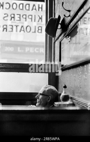 Charley's Dining Rooms in the City of London 1960er. Auf der Speisekarte - auf das Fenster gemalt sind Schellfisch, Kippers, Bloater. (Bloater sind eine Art kaltgeräucherter Hering.) Sie werden leicht geraucht, ohne auszunehmen, was einen charakteristischen, leicht geilen Geschmack verleiht. Wenn man darauf wartet, dass sein Mittagessen serviert wird, und an einem Tisch mit hoher Rückenlehne sitzt, hängt ein Mann seinen Trilby-Hut auf einen Stift über seinem Kopf. London, England, ca. 1969. HOMER SYKES AUS GROSSBRITANNIEN Stockfoto