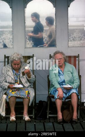 Brighton Palace Pier, zwei Seniorinnen Lder Ladies essen Teller mit Essen und ein Eis Brighton East Sussex, England um 1985. HOMER SYKES AUS DEN 1980ER JAHREN Stockfoto